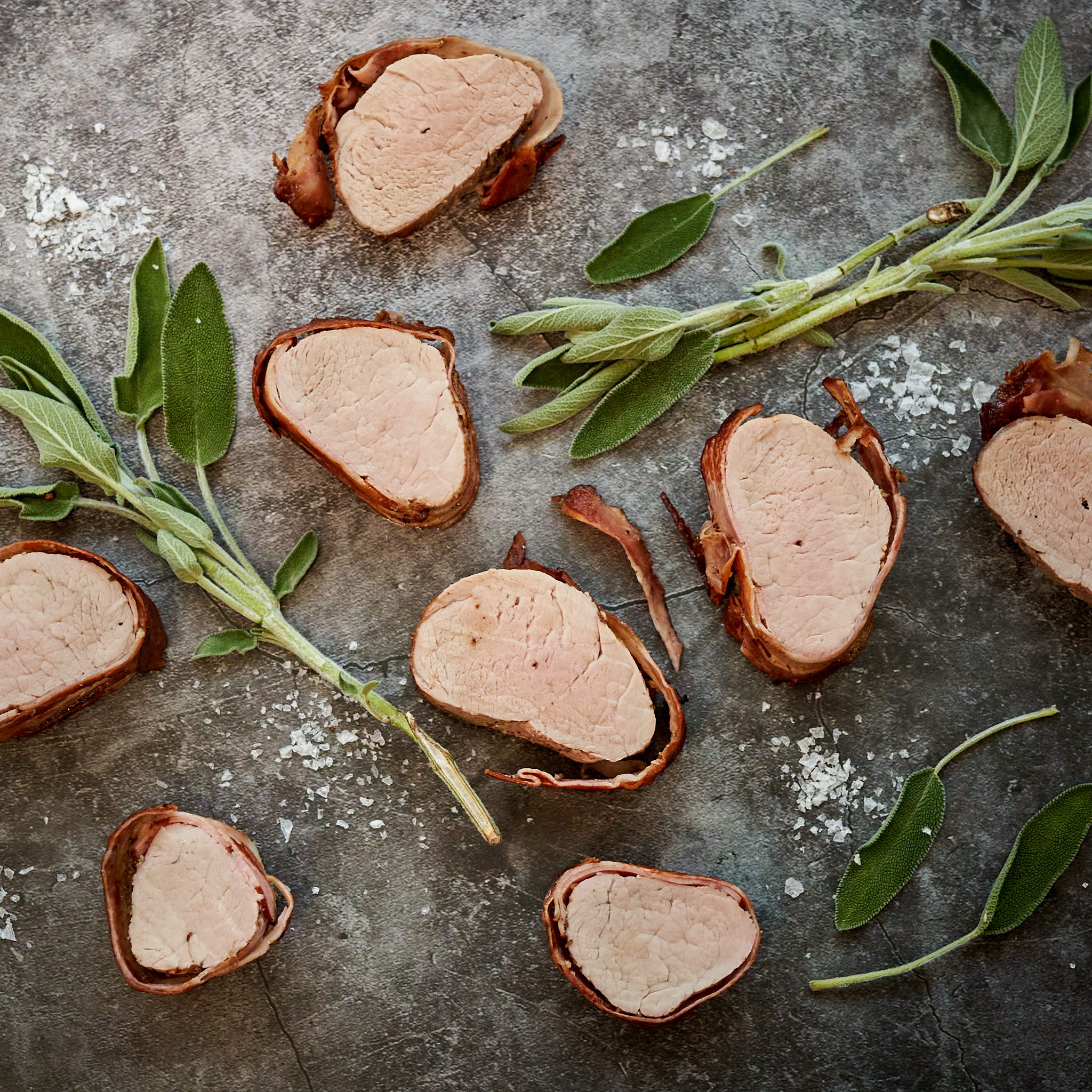 Gebratene Filetstücke vom Strohschwein auf Marmorplatte mit Salbei-Büdel arrangiert 