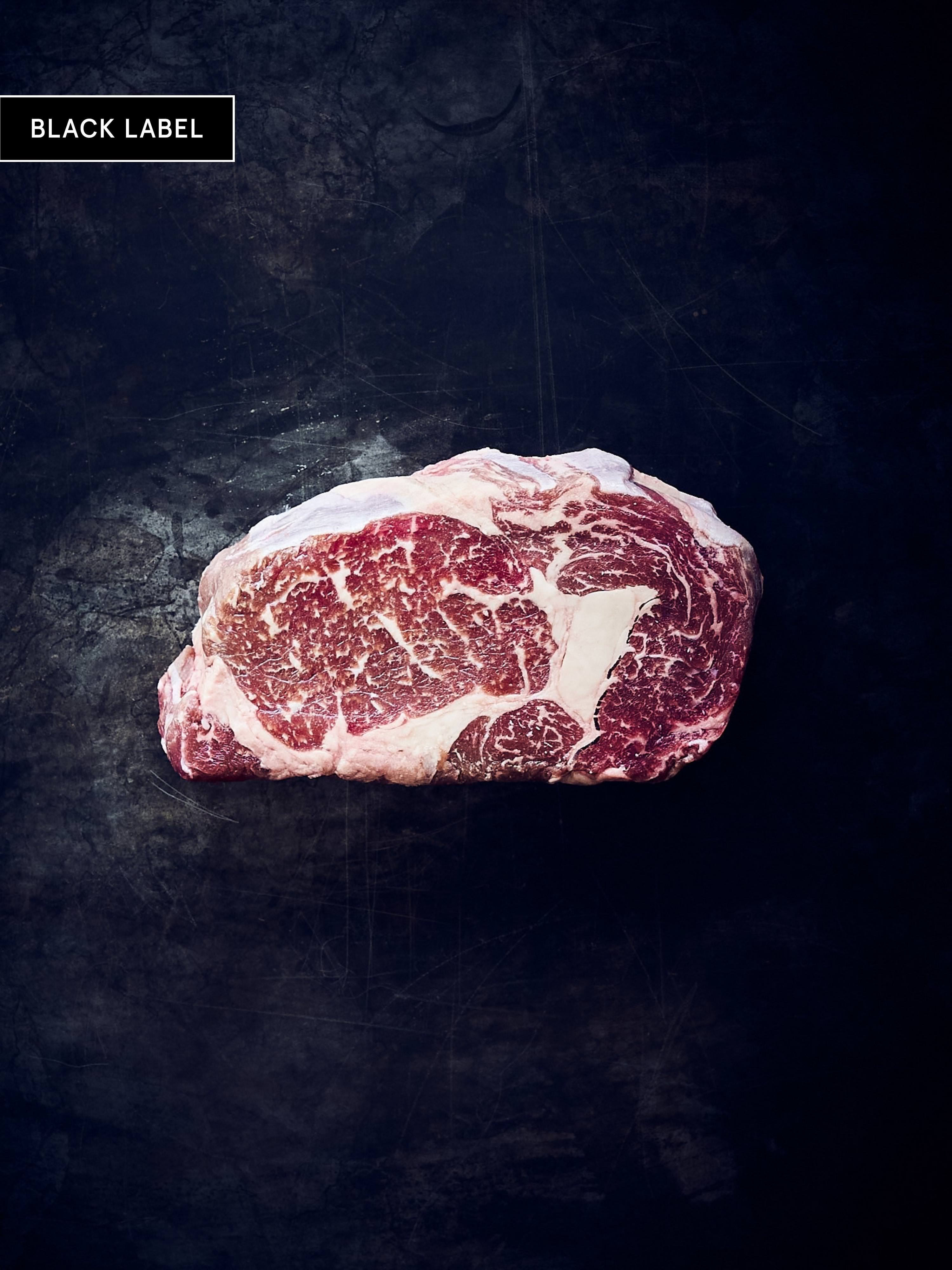 Stark marmoriertes Fitmeat Black Label Rib Eye Steak auf schwarzem Hintergrund