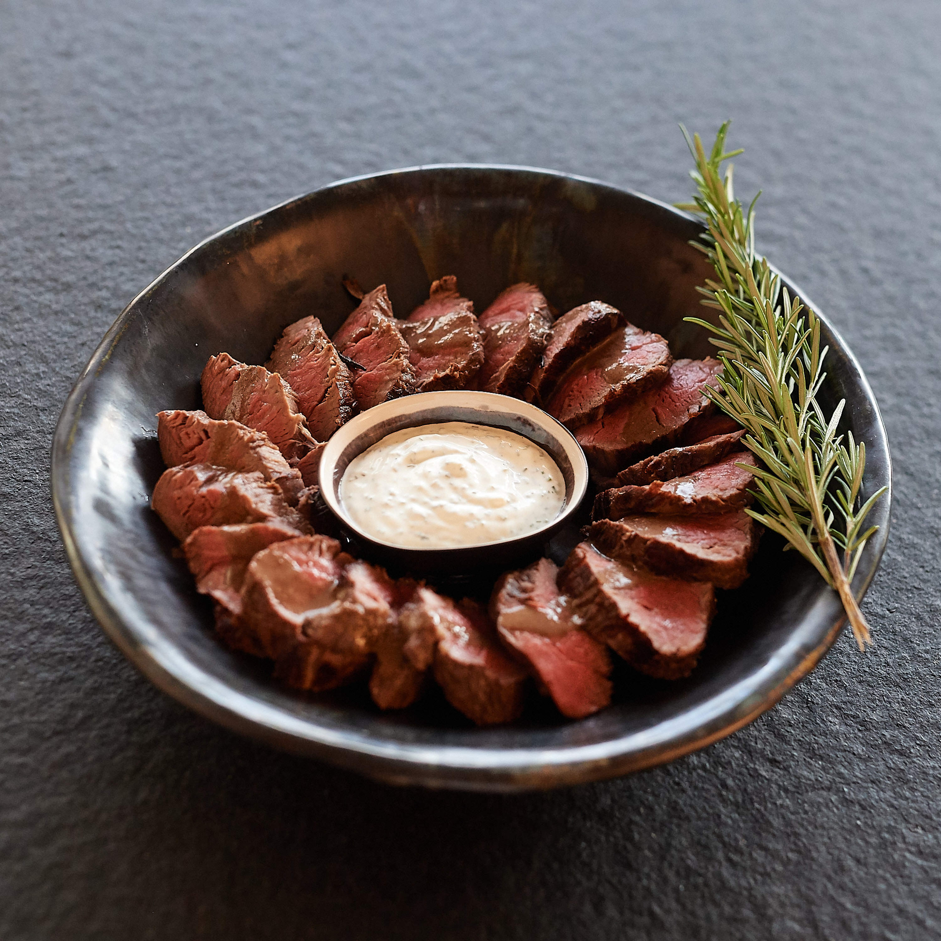 Rinderfiletstreifen in schwarzer Schuessel mit Sauce Rinderfiletstreifen in schwarzer Schuessel mit Sauce