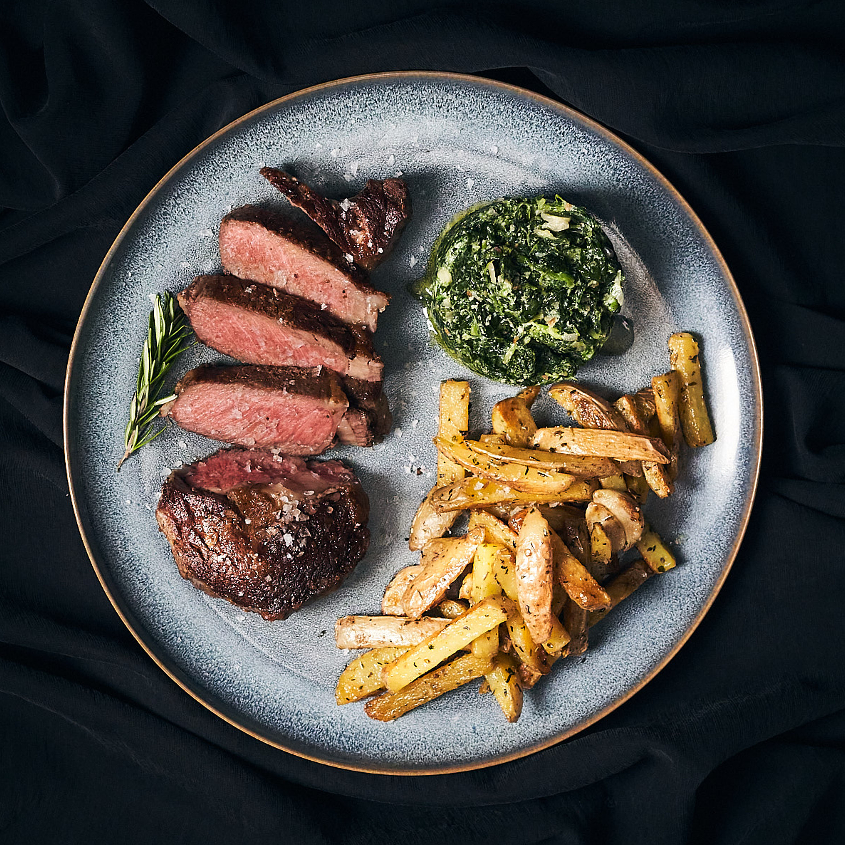 Gegrilltes Rib-Eye Steak mit rosa Kern serviert mit Steak-Fries und Spinat Gegrilltes Rib-Eye Steak mit rosa Kern serviert mit Steak-Fries und Spinat